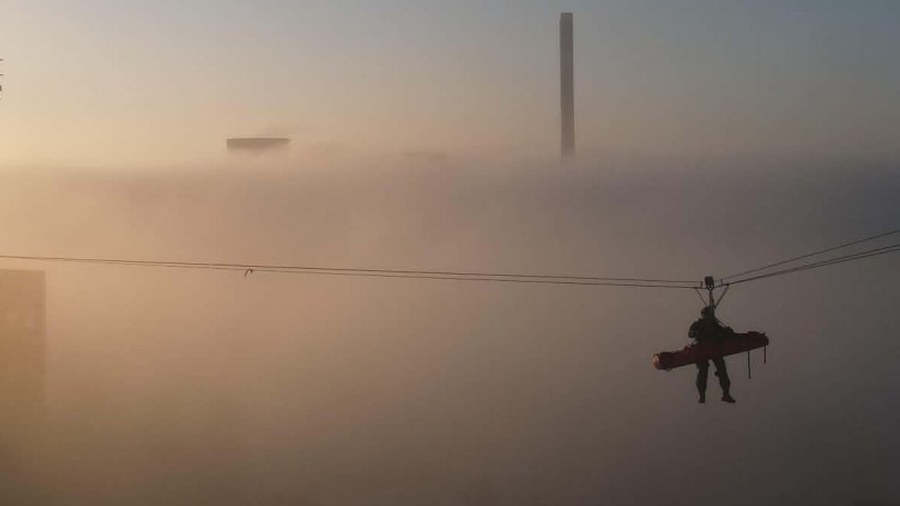 Retter mit Schleifkorbtrage an der Schrägseilstrecke über einem Förderturm im Morgennebel